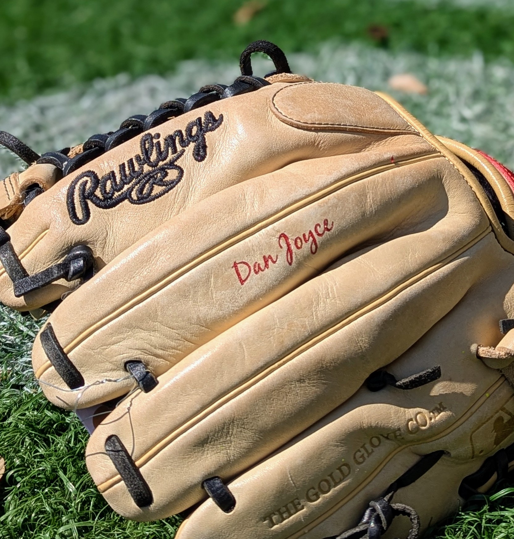 Red cursive name engraved on middle finger of tan Rawlings outfield glove
